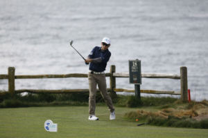 Evan Koutsopetras swinging a golf club by the water on the 18th hole