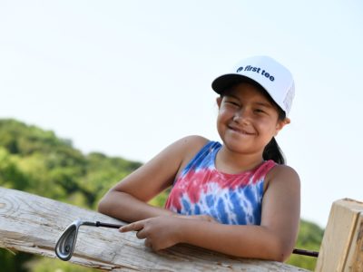 First Tee participant posing with a golf club by a fence.